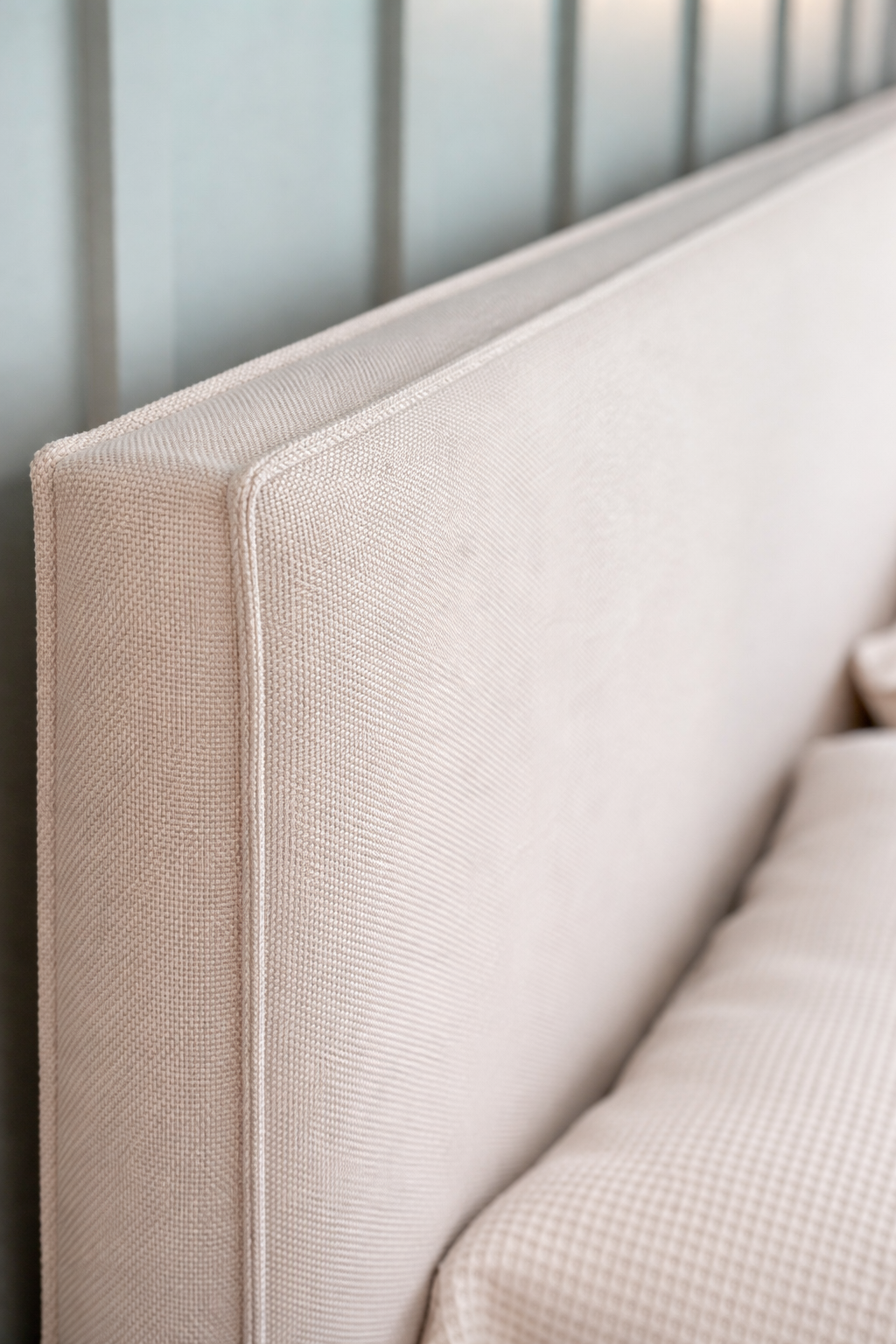 Close-up of a beige upholstered headboard with a neutral background