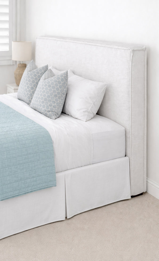 White upholstered bed with light gray and white pillows in a minimalistic bedroom.