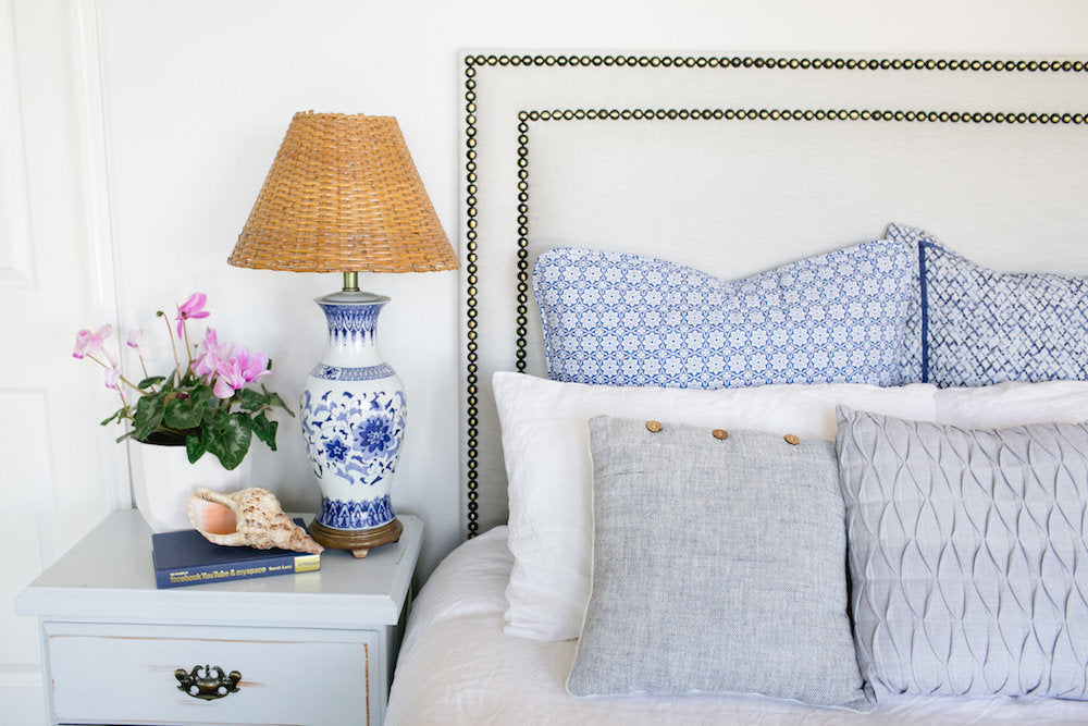 Bedroom with a bed featuring patterned and plain pillows, a lamp, and a small plant on a nightstand.