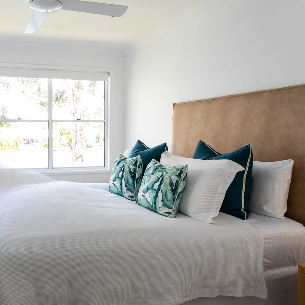 Bedroom with a bed featuring decorative pillows near a window.